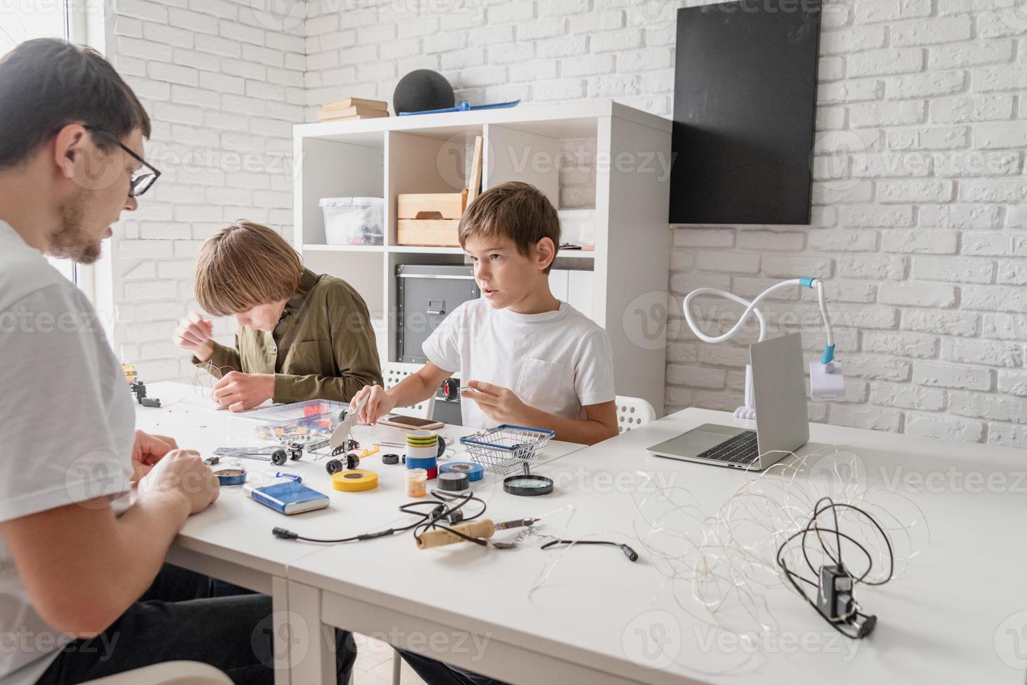 meninos e professor se divertindo construindo carros robôs na oficina foto