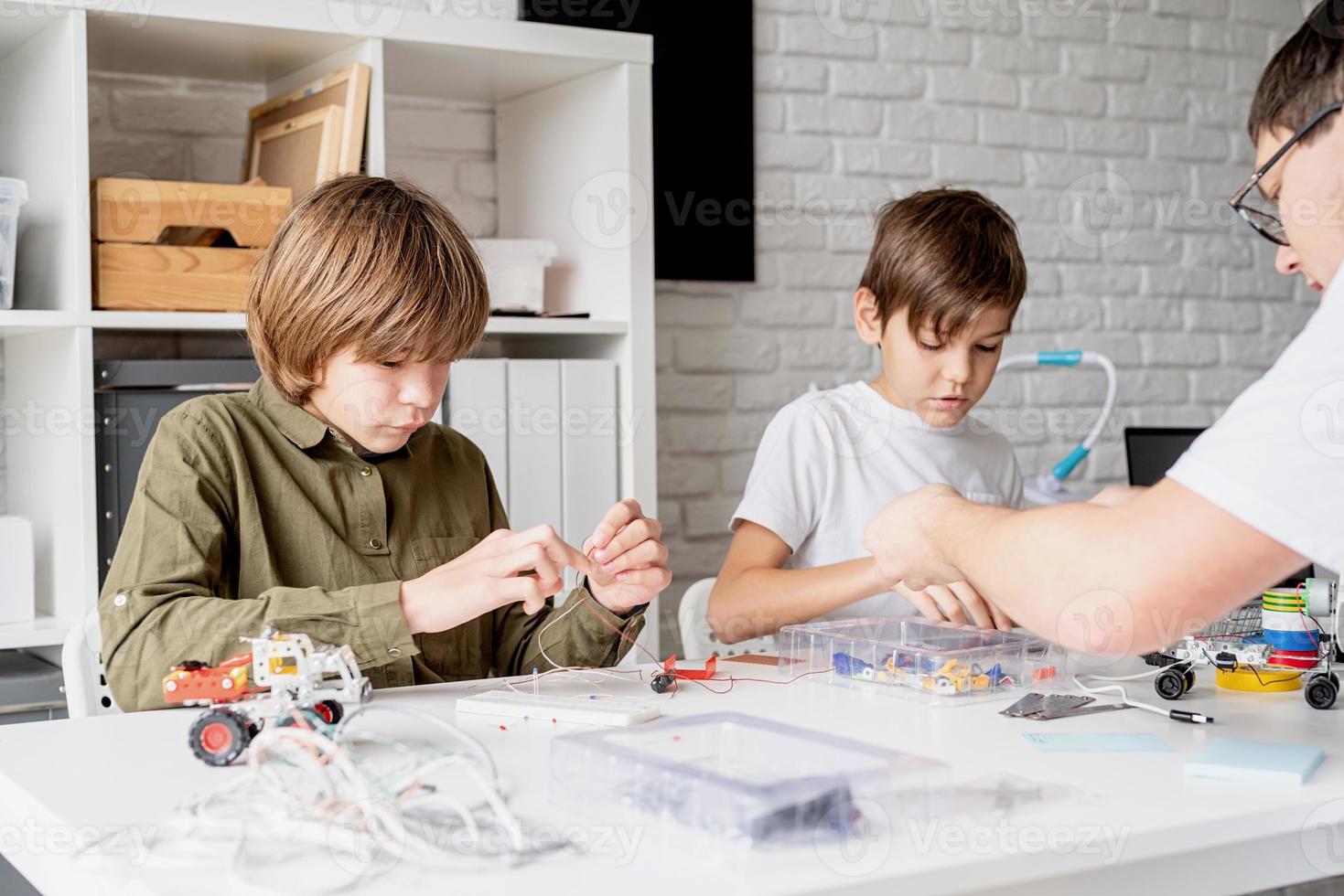 meninos e professor se divertindo construindo carros robôs na oficina foto