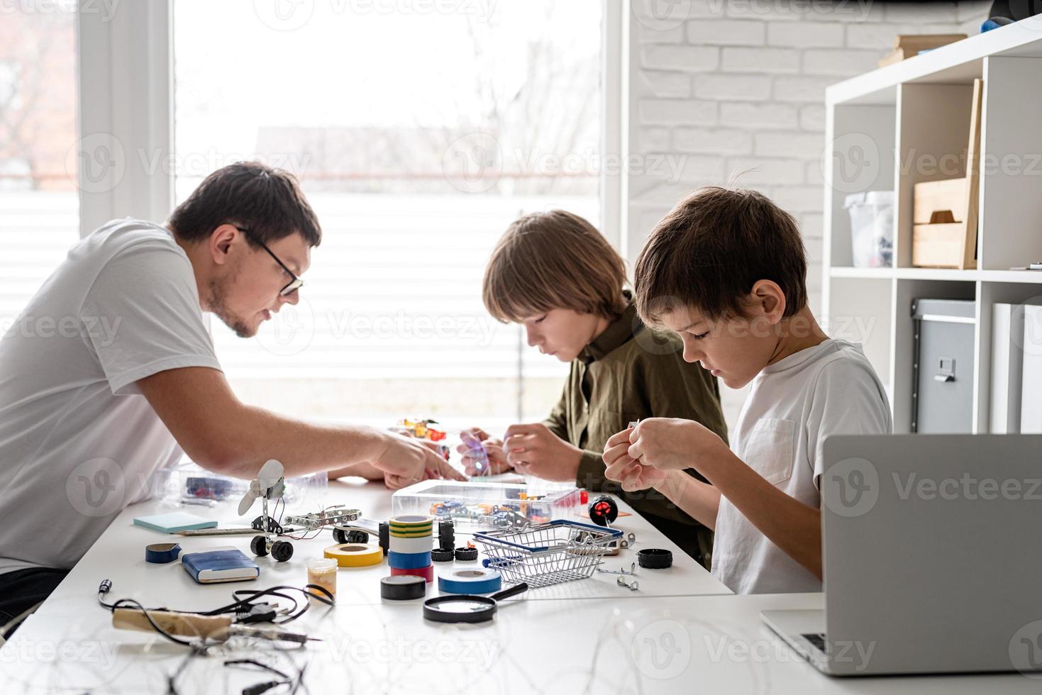 meninos e professor se divertindo construindo carros robôs na oficina foto