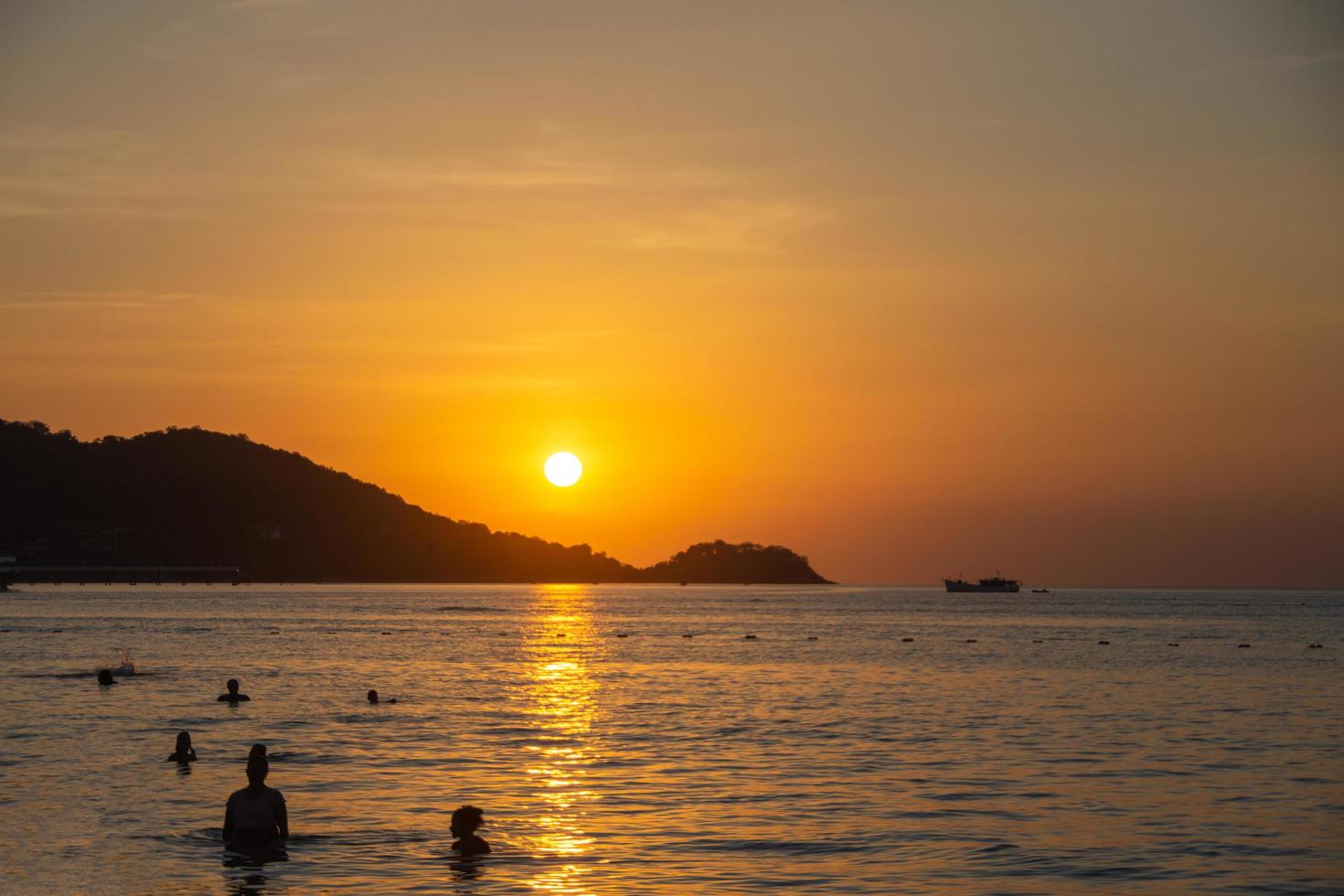 pessoas nadando no belo pôr do sol em patong beach, phuket, tailândia foto