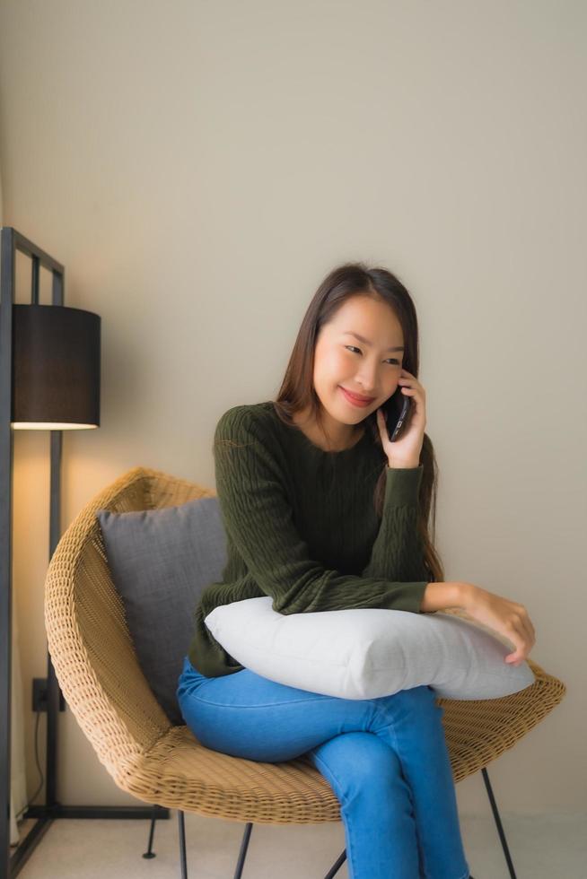 retrato de belas jovens mulheres asiáticas usando um telefone celular e sentado na cadeira do sofá foto