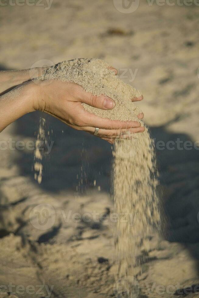 fechar-se do mãos com areia queda em uma de praia foto