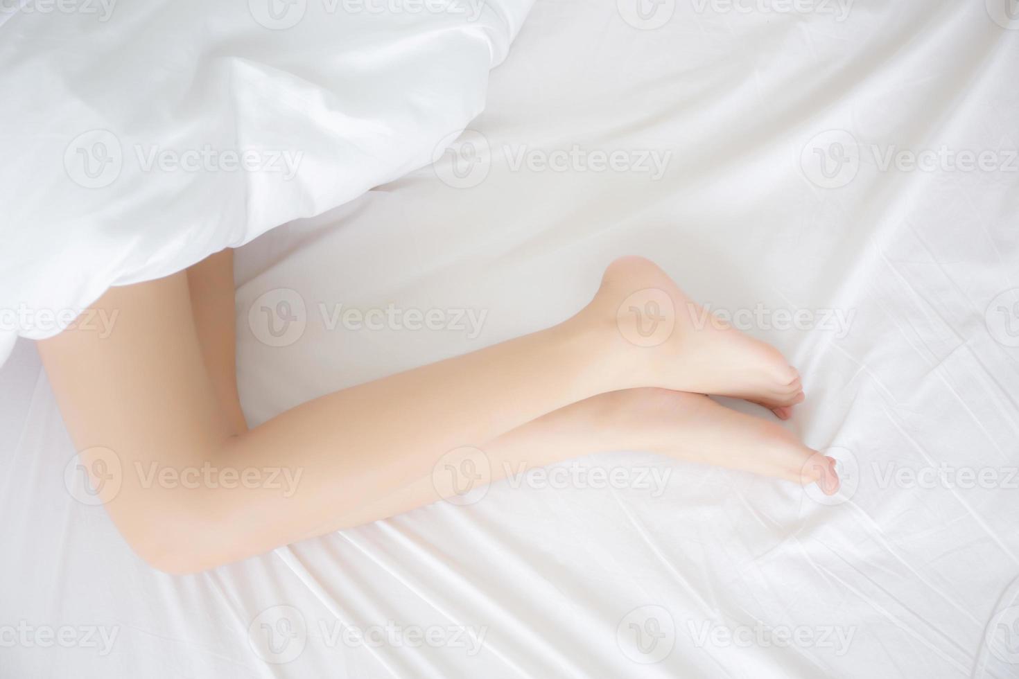 bela perfeita de pernas de mulher slim sexy na cama no quarto, pele lisa de beleza garota pés cuidados de saúde, conforto e bem-estar, sono deitado feminino para relaxar com cobertor, conceito de estilo de vida. foto