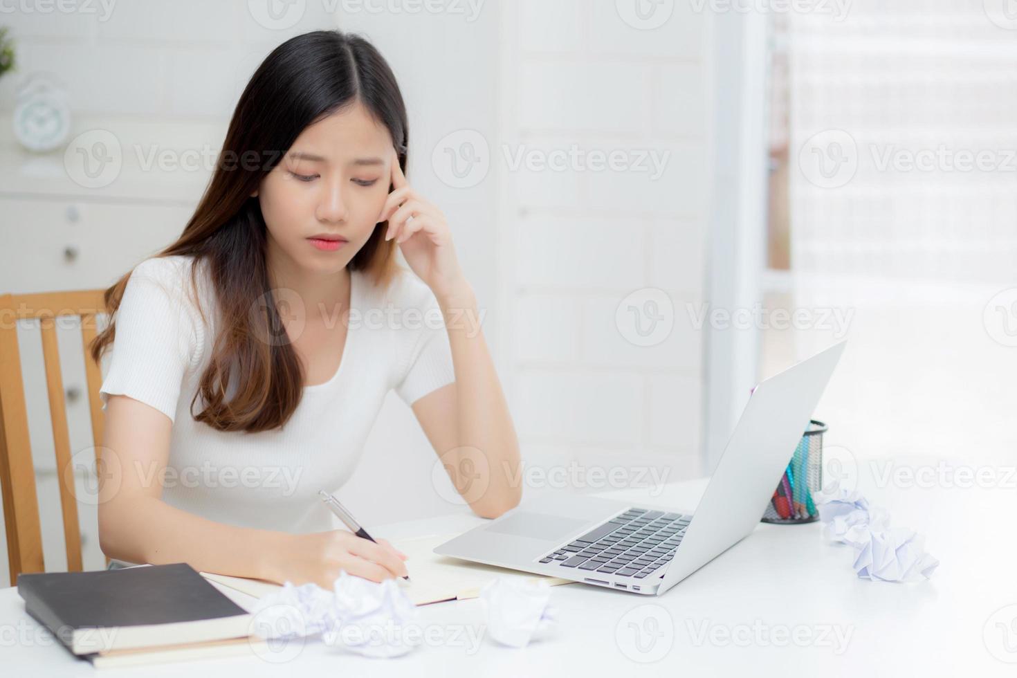 jovem mulher asiática que trabalha com computador portátil pensa projeto de ideia e papel amassado tendo o problema na mesa em casa, garota usando notebook com conceito frustrado e problemas, negócios e freelance. foto