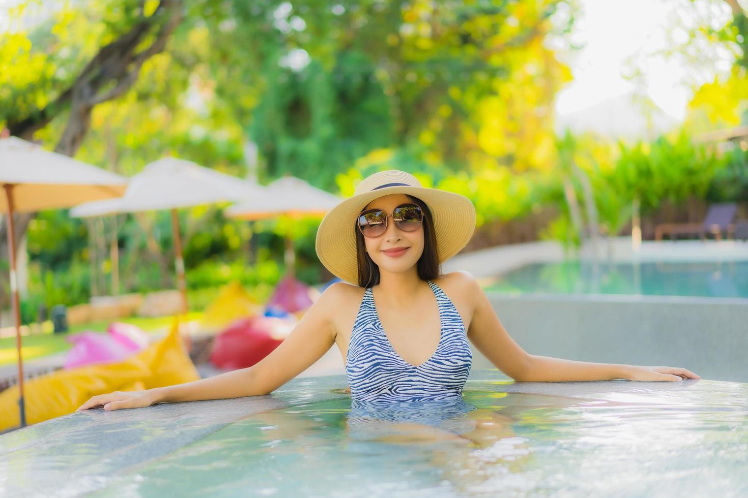 lindas jovens mulheres asiáticas sorriso feliz relaxando ao redor da piscina ao ar livre em hotel resort para viagens de férias foto