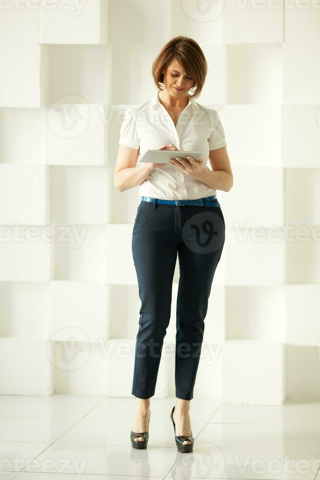 empresária em pé contra branco parede enquanto olhando às tábua foto