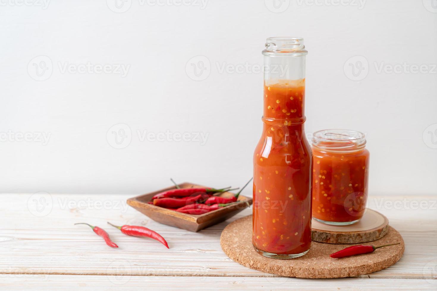 pimenta ou molho de pimenta em garrafa e jarra com fundo de madeira foto