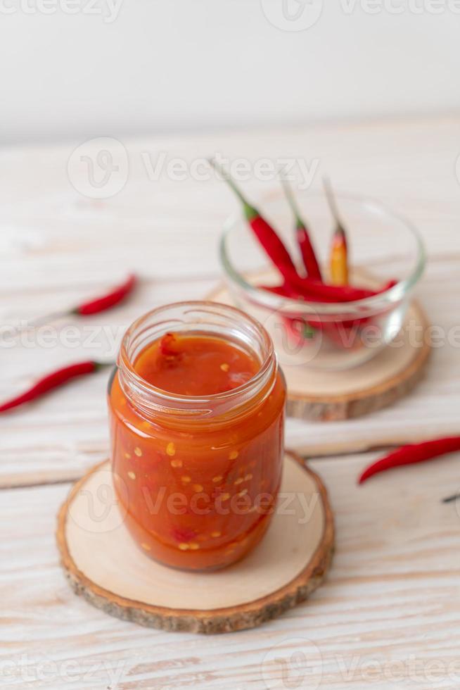 pimenta ou molho de pimenta em garrafa e jarra com fundo de madeira foto