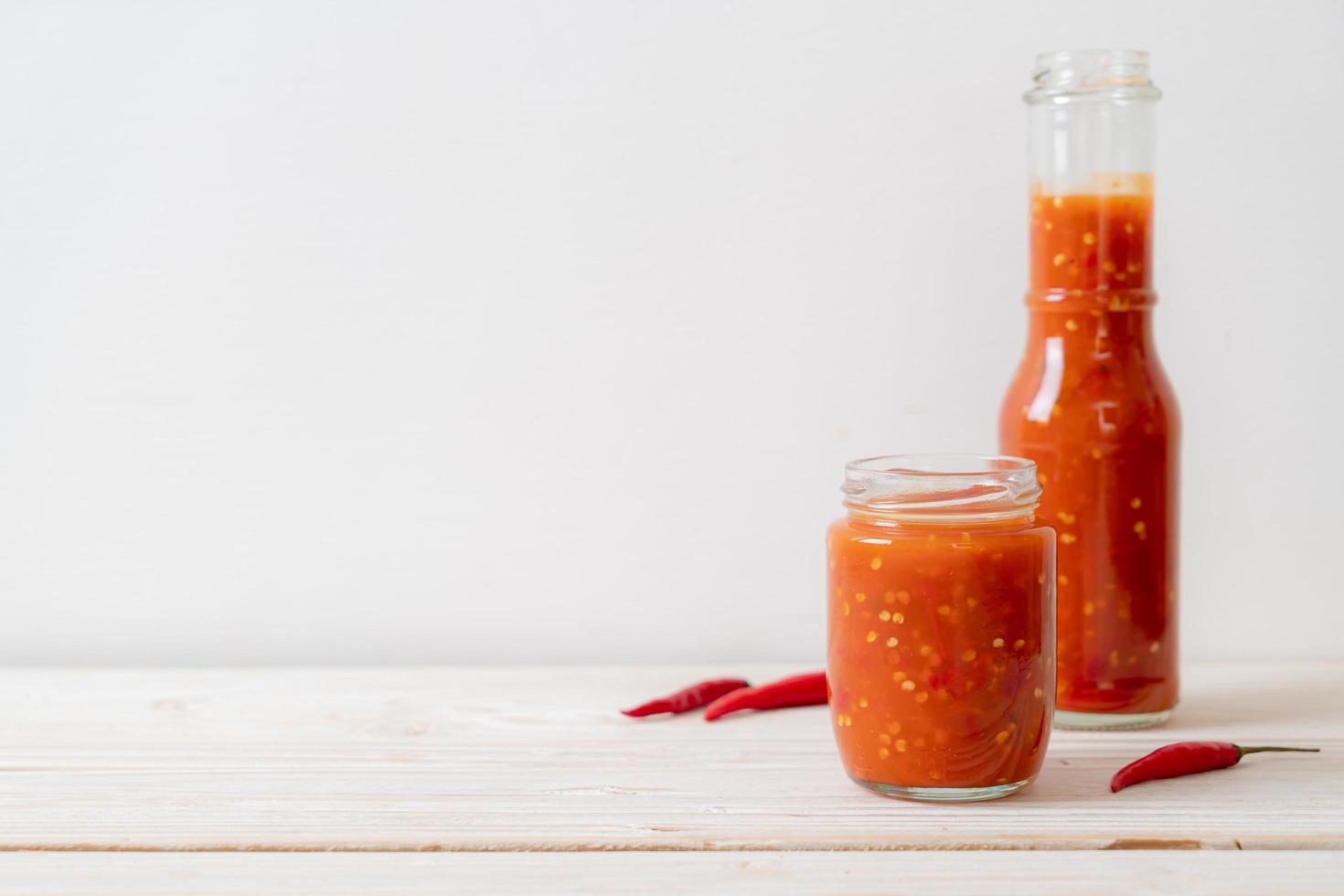 pimenta ou molho de pimenta em garrafa e jarra com fundo de madeira foto