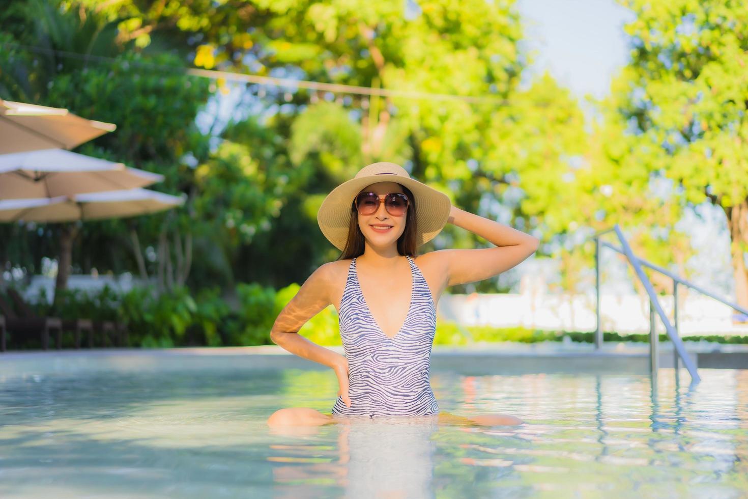 lindas jovens mulheres asiáticas sorriso feliz relaxando ao redor da piscina ao ar livre em hotel resort para viagens de férias foto