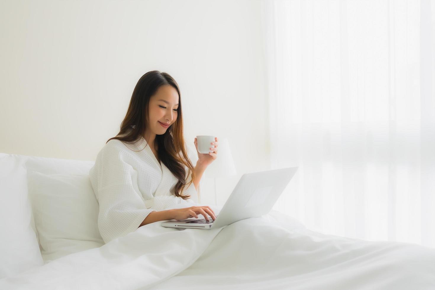 retrato de belas jovens mulheres asiáticas com uma xícara de café e um laptop na cama foto