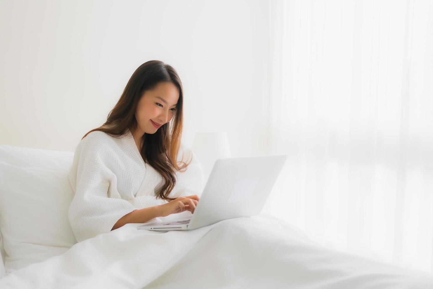 retrato de belas jovens mulheres asiáticas com uma xícara de café e um laptop na cama foto