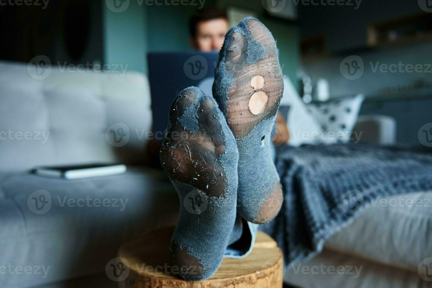 homem com gotejante meias em repouso em sofá, usando computador portátil foto