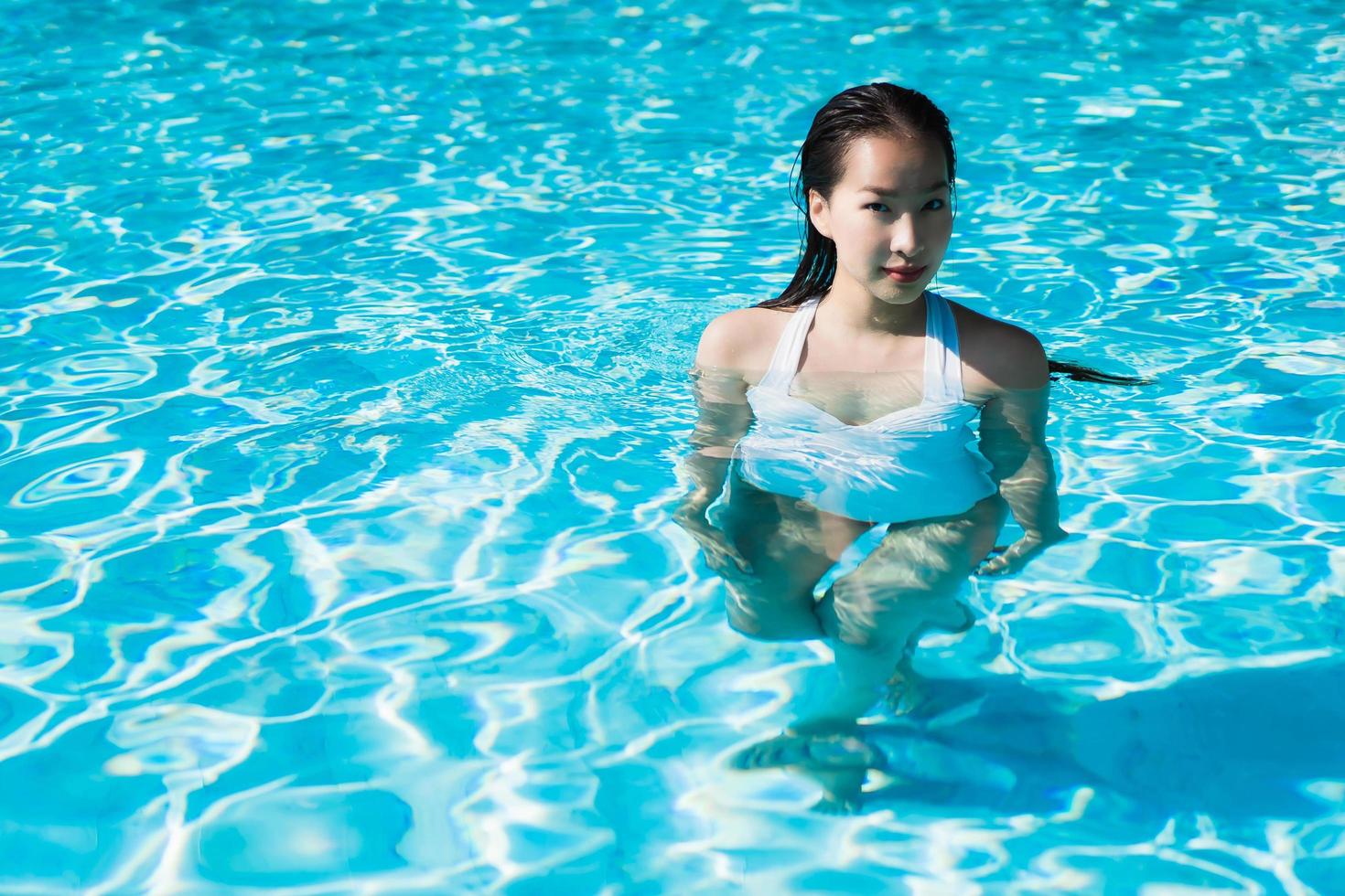 bela jovem asiática feliz e sorrindo na piscina para relaxar, viagens e férias foto