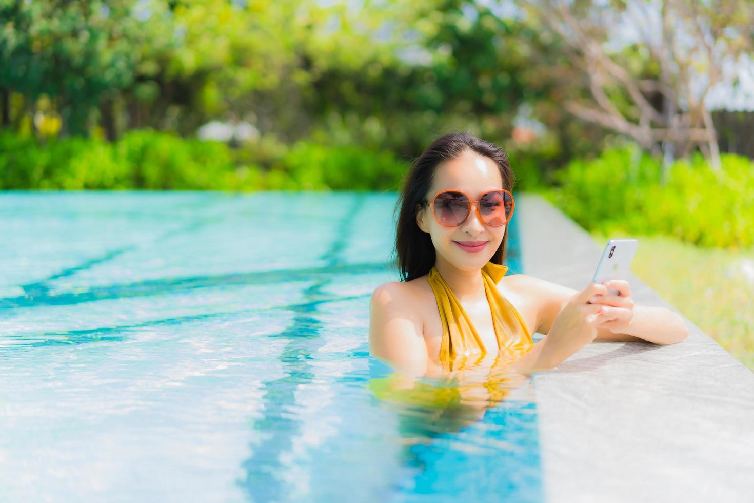 retrato bela jovem asiática usando telefone celular ou celular na piscina foto