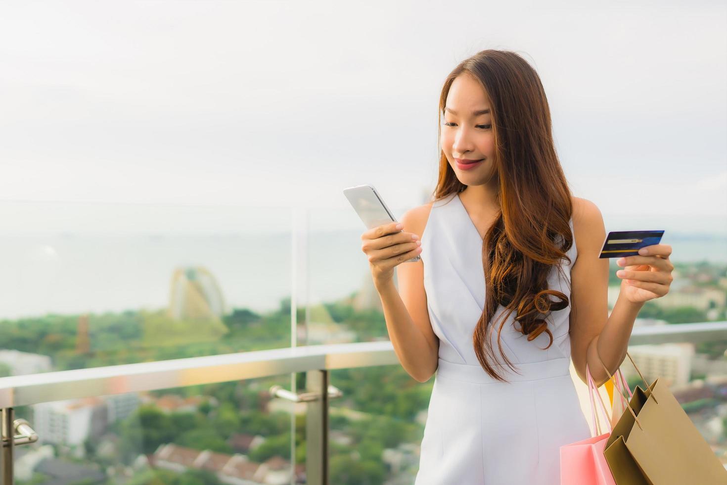 retrato linda jovem asiática feliz e sorrindo com cartão de crédito e celular ou telefone inteligente e sacola de compras foto