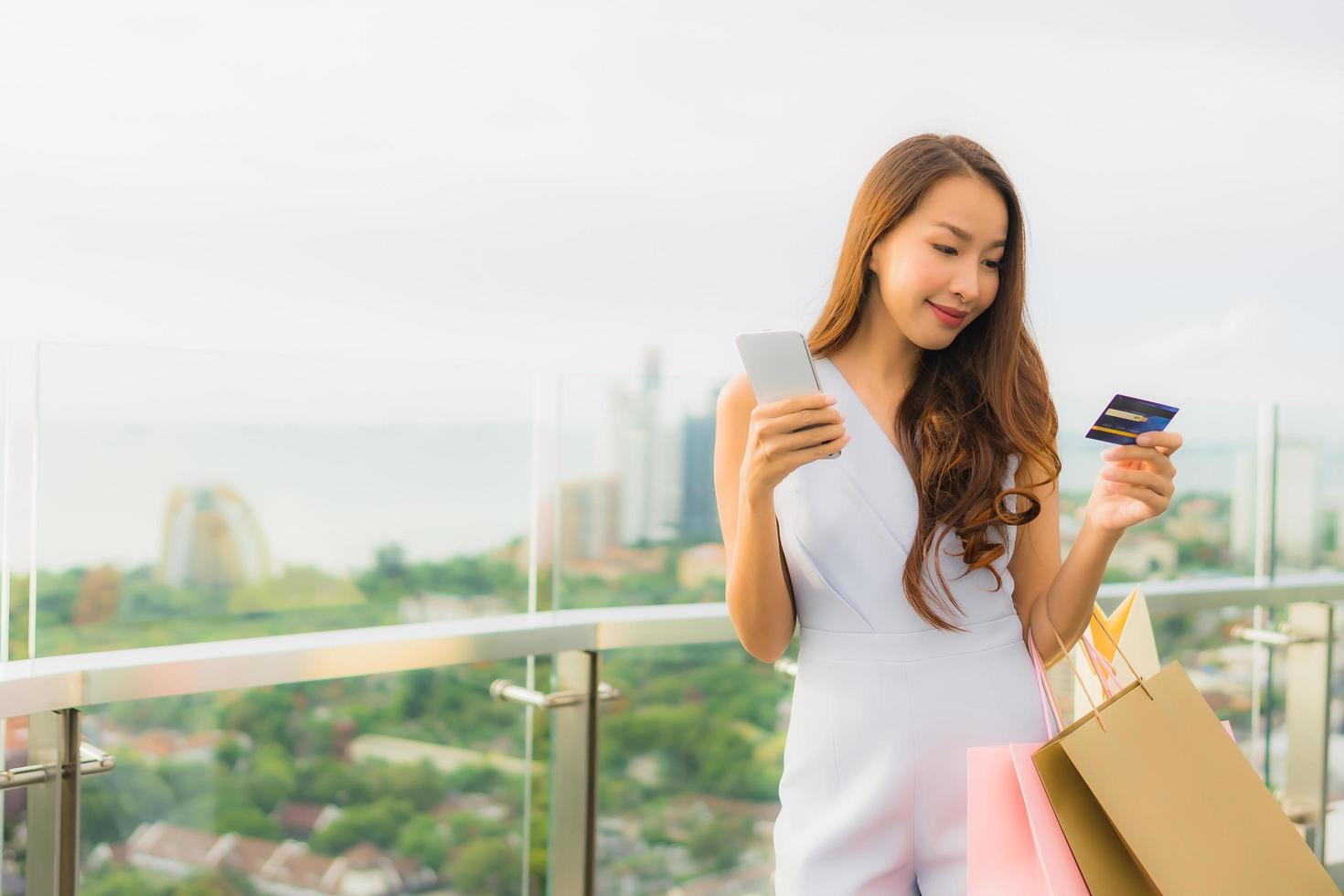 retrato linda jovem asiática feliz e sorrindo com cartão de crédito e celular ou telefone inteligente e sacola de compras foto
