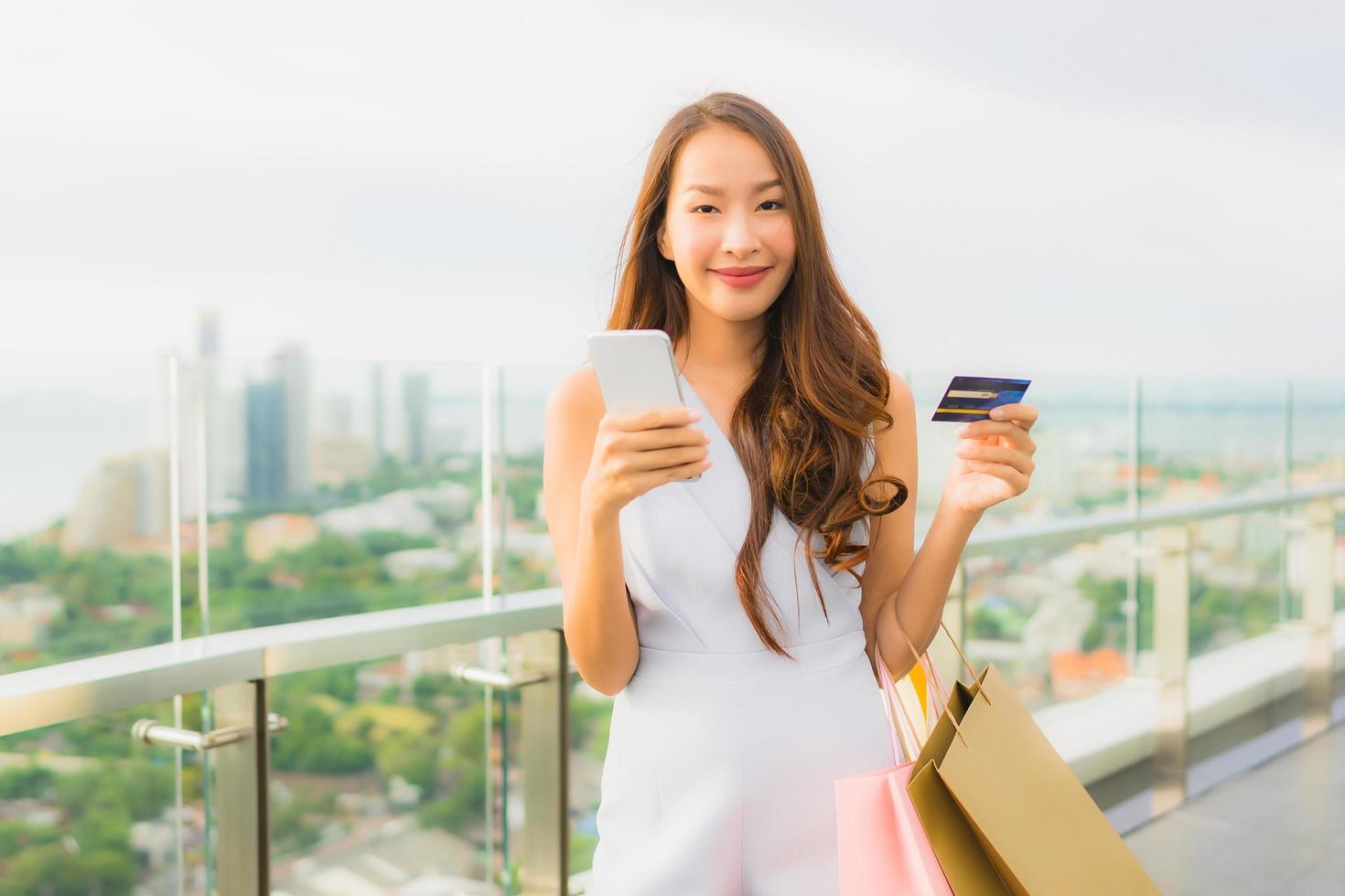 retrato linda jovem asiática feliz e sorrindo com cartão de crédito e celular ou telefone inteligente e sacola de compras foto