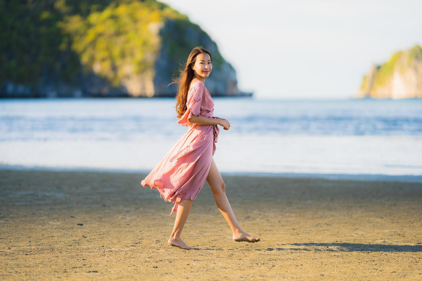 retrato jovem linda mulher asiática andar sorrindo e feliz na praia, mar e oceano foto