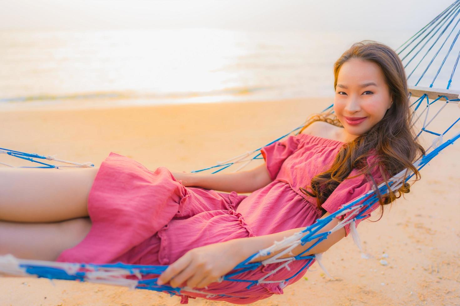 retrato linda jovem asiática sentada na rede com um sorriso feliz perto da praia, mar e oceano foto