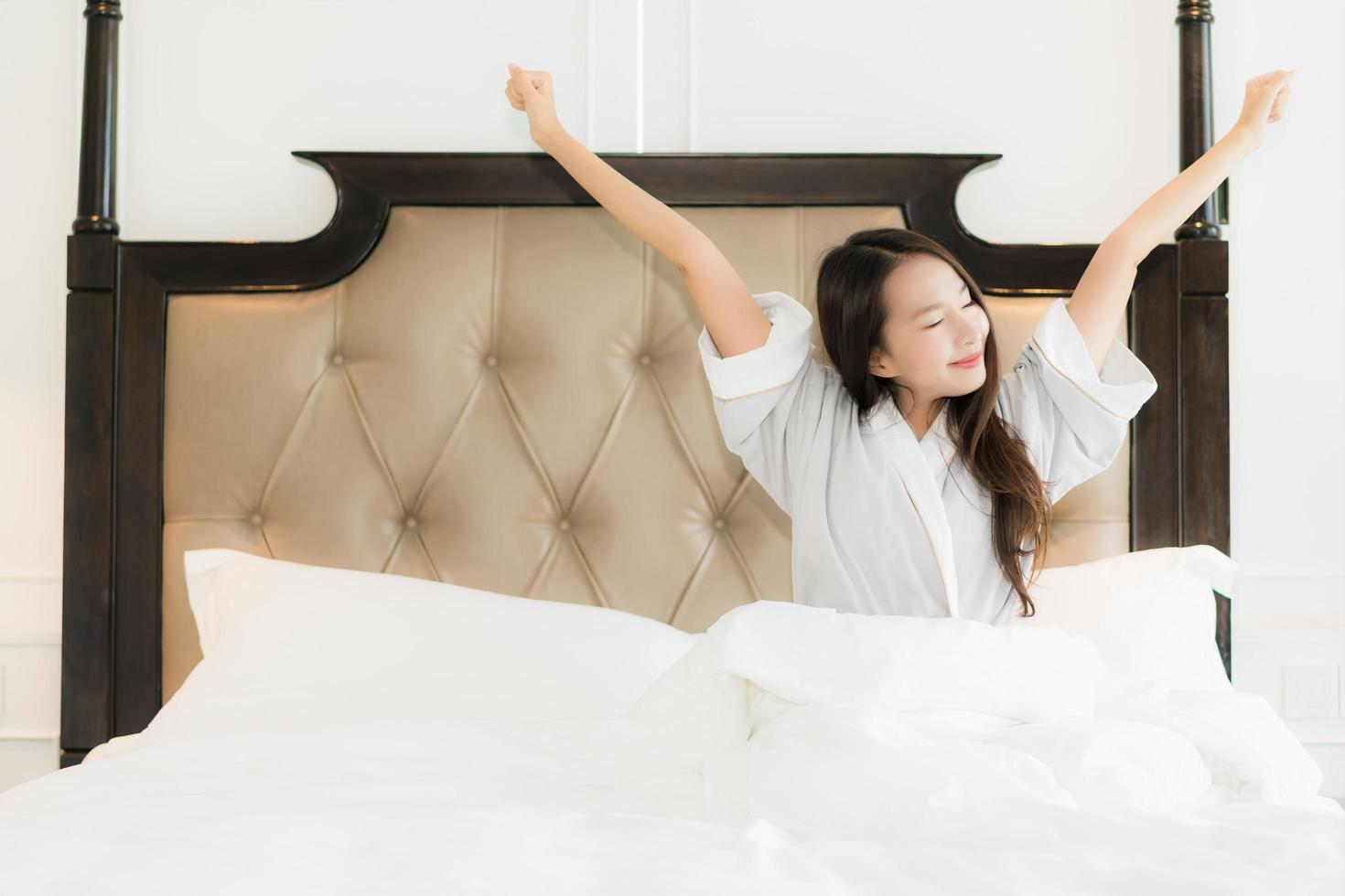 retrato bela jovem asiática acordar feliz e sorrir na cama, no interior do quarto foto