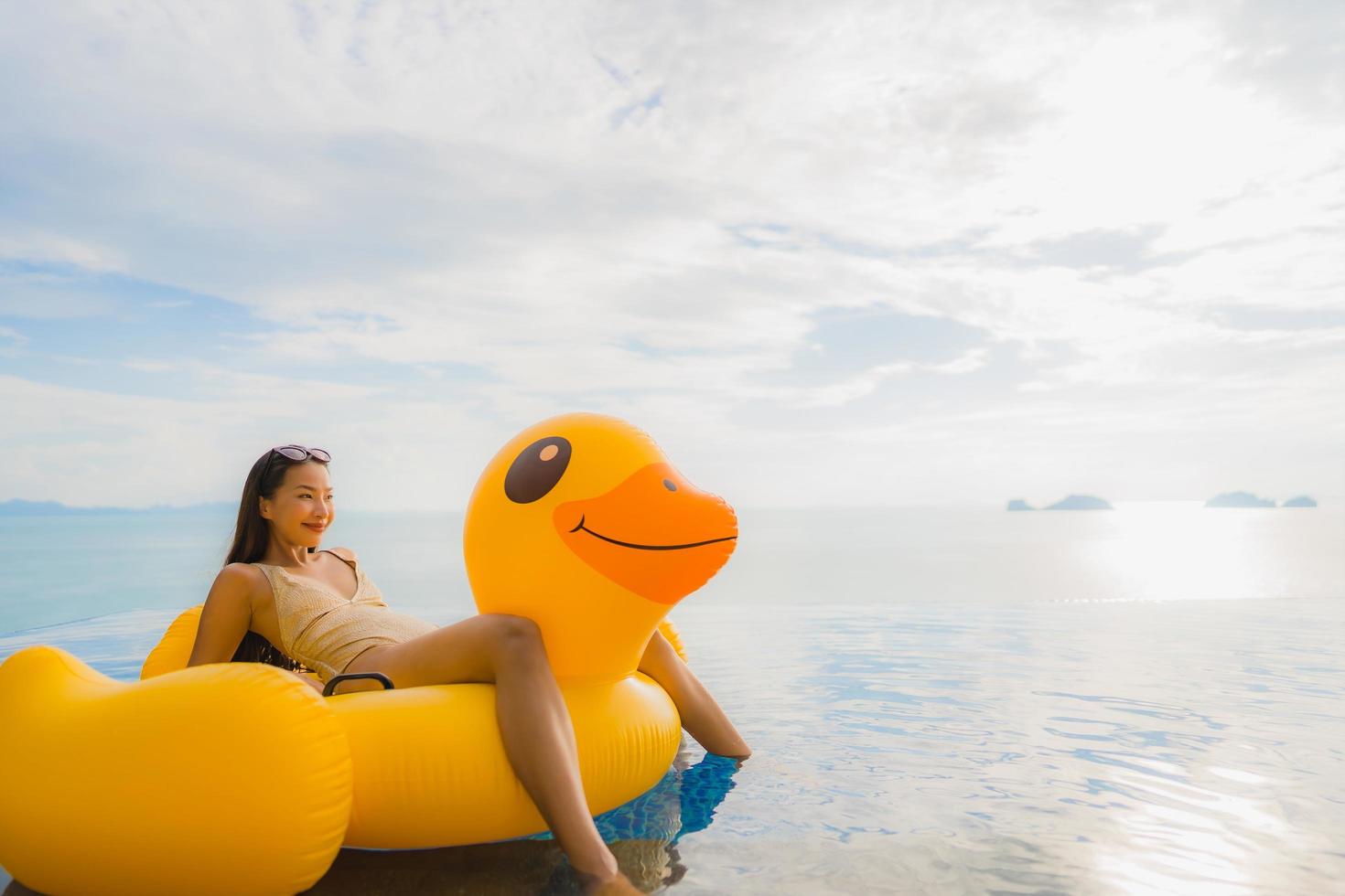 retrato de jovem mulher asiática em pato inflável flutuante amarelo ao redor de piscina externa em hotel e resort foto