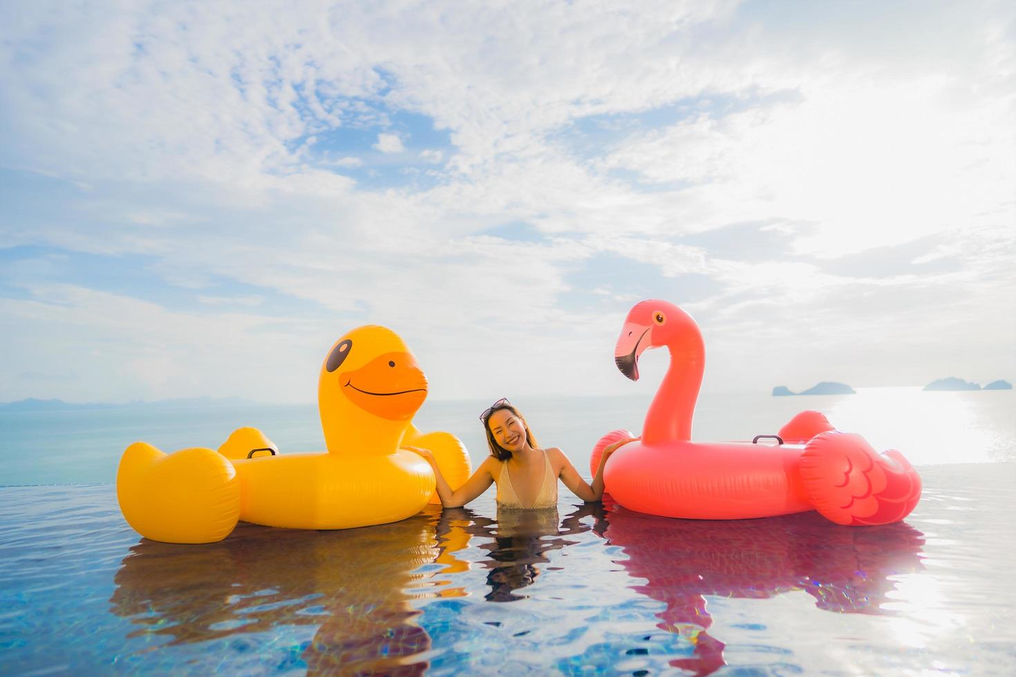 retrato jovem mulher asiática em pato inflável flutuante amarelo e flamingo rosa ao redor de piscina externa em hotel e resort foto