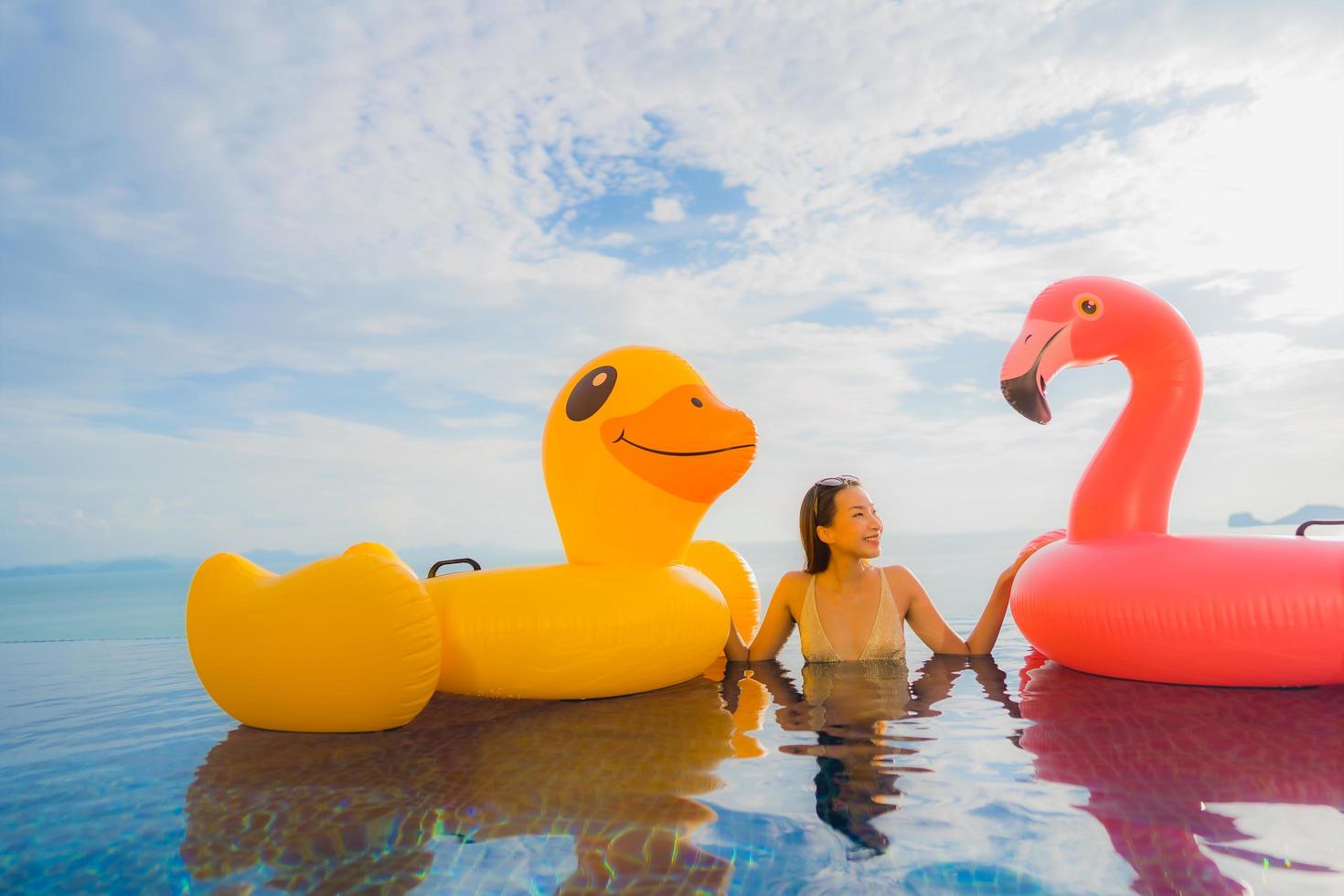 retrato jovem mulher asiática em pato inflável flutuante amarelo e flamingo rosa ao redor de piscina externa em hotel e resort foto