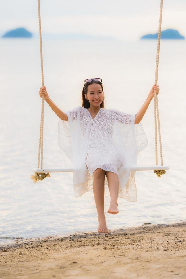 retrato linda jovem asiática sentada no balanço ao redor da praia, mar, oceano, para relaxar foto
