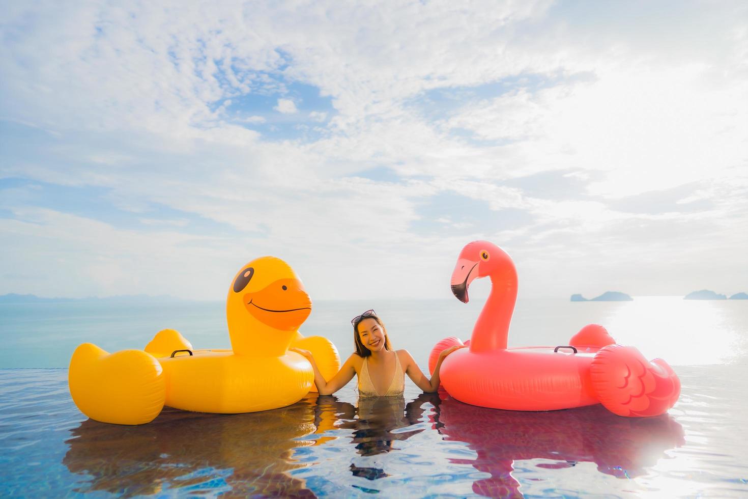 retrato jovem mulher asiática em pato inflável flutuante amarelo e flamingo rosa ao redor de piscina externa em hotel e resort foto