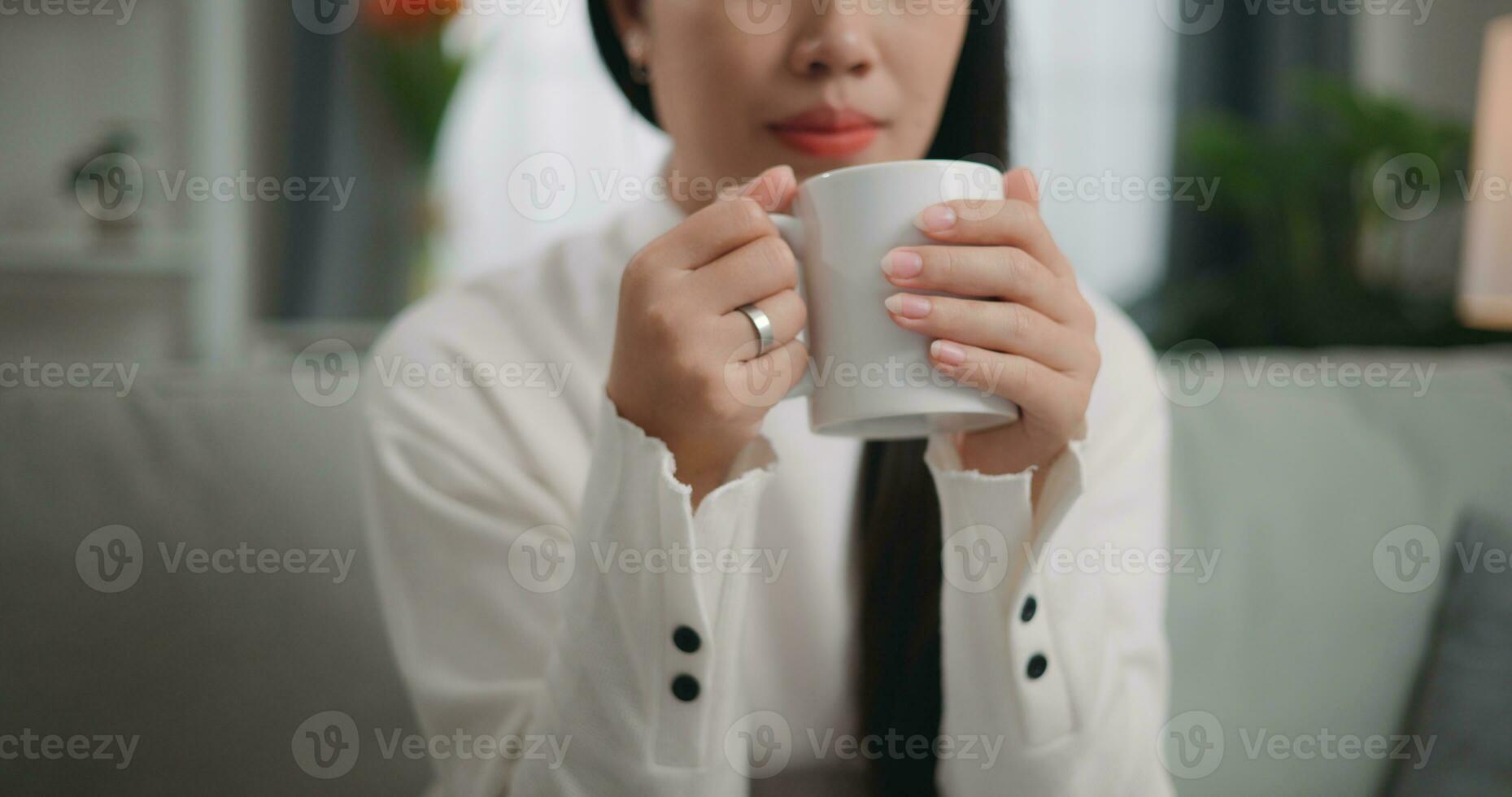 ásia mulher bebendo uma café enquanto sentado em a sofá foto