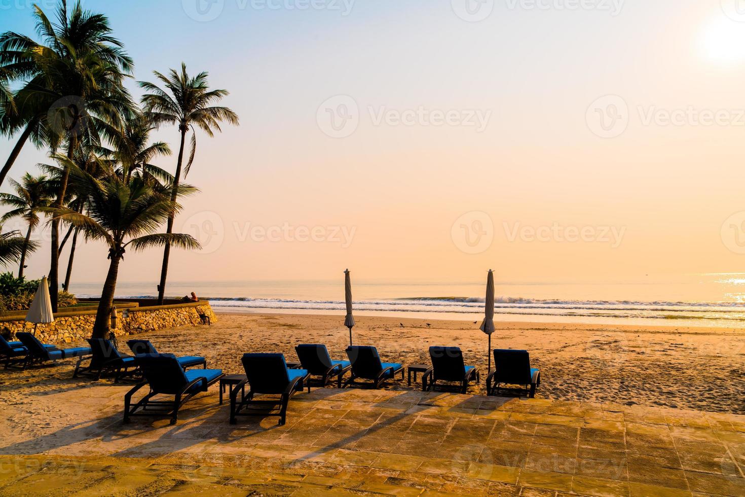 cadeira de praia guarda-sol com palmeira e praia do mar na hora do nascer do sol - conceito de férias e feriados foto