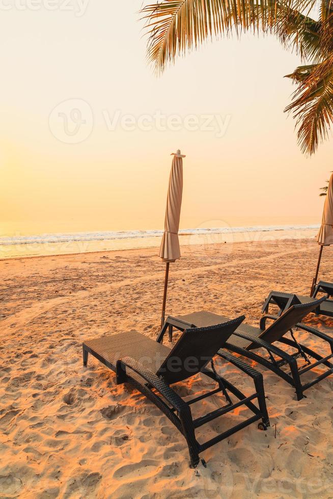 cadeira de praia guarda-sol com palmeira e praia do mar na hora do nascer do sol - conceito de férias e feriados foto
