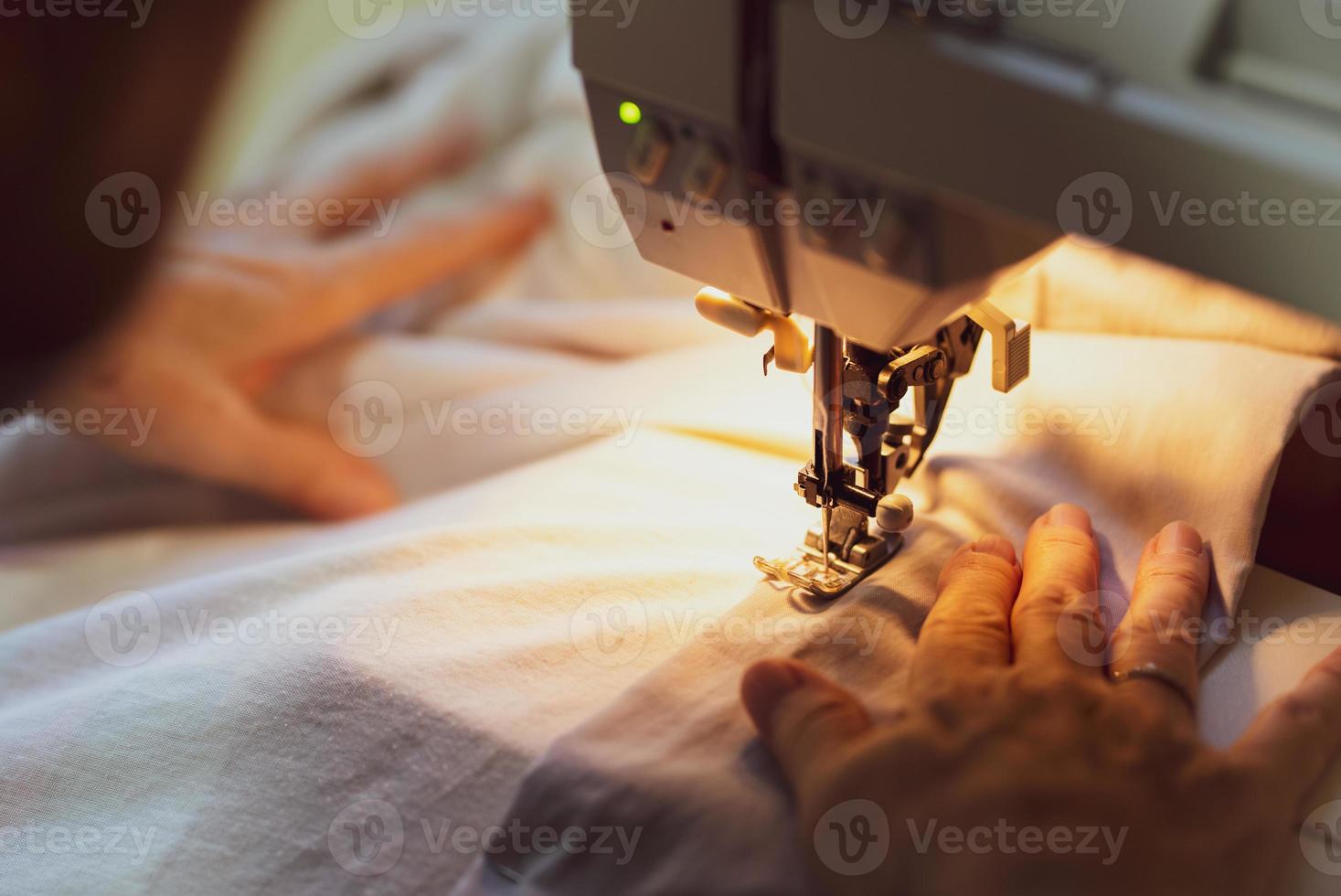feche as mãos da mulher sênior usando a máquina de costura para costurar roupas em casa foto