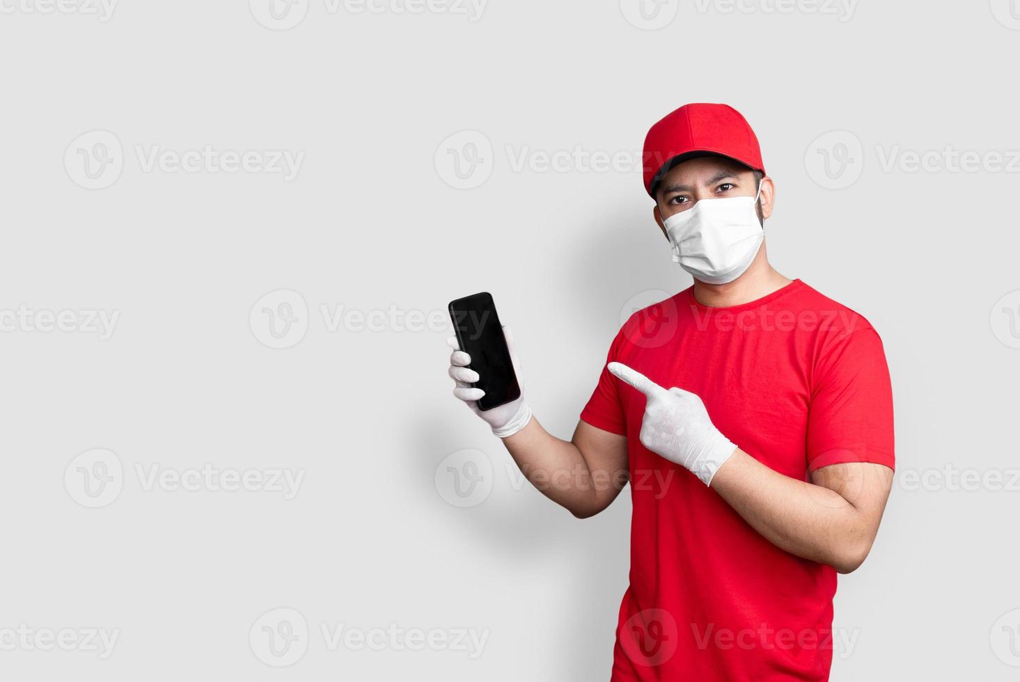 entregador empregado com tampa vermelha máscara em branco uniforme uniforme segurar aplicativo preto para celular isolado no fundo branco foto