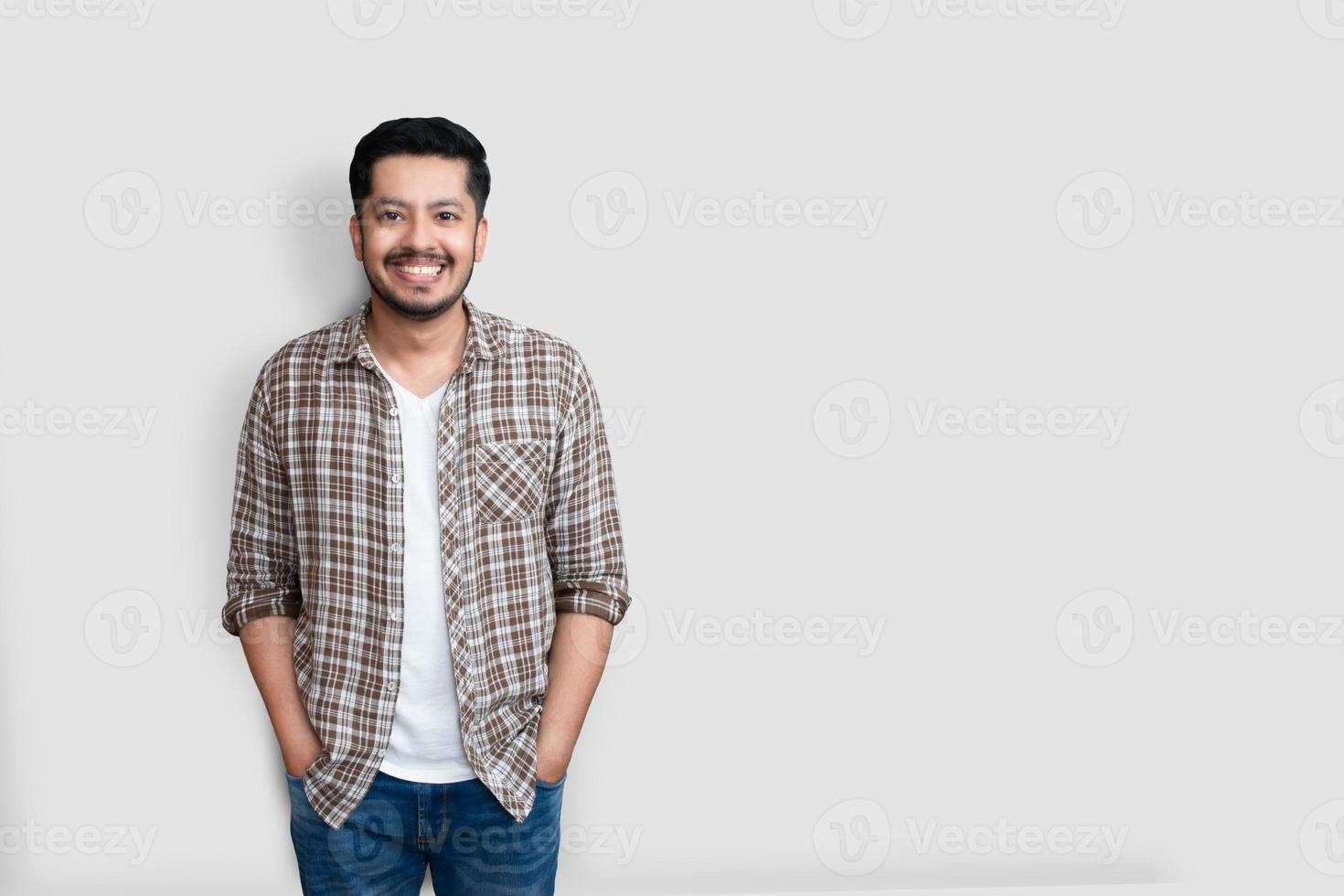 atraente bonito positivo feliz homem asiático. lindo paquistanês asiático vestindo uma camisa xadrez marrom com um grande sorriso isolado no fundo branco foto