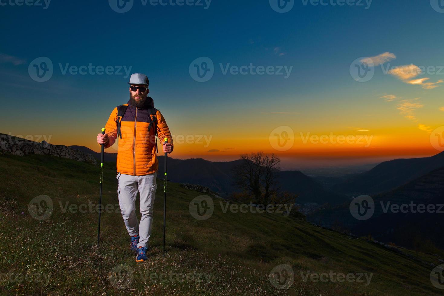 jovem com barba praticando caminhada nórdica em um pôr do sol colorido foto