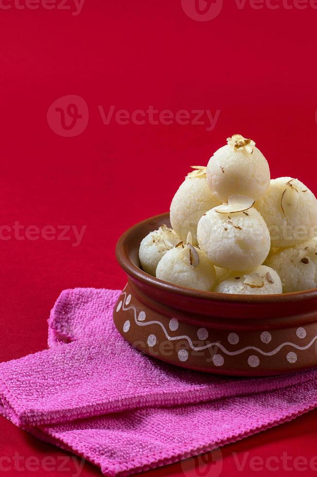 doce indiano ou sobremesa - rasgulla, famoso doce bengali em tigela de barro com guardanapo sobre fundo vermelho foto