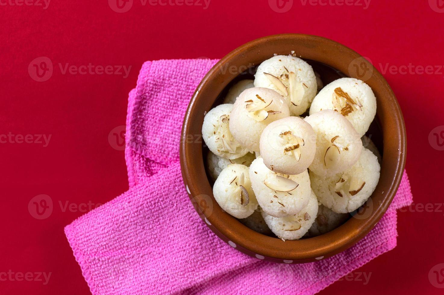 doce indiano ou sobremesa - rasgulla, famoso doce bengali em tigela de barro com guardanapo sobre fundo vermelho foto
