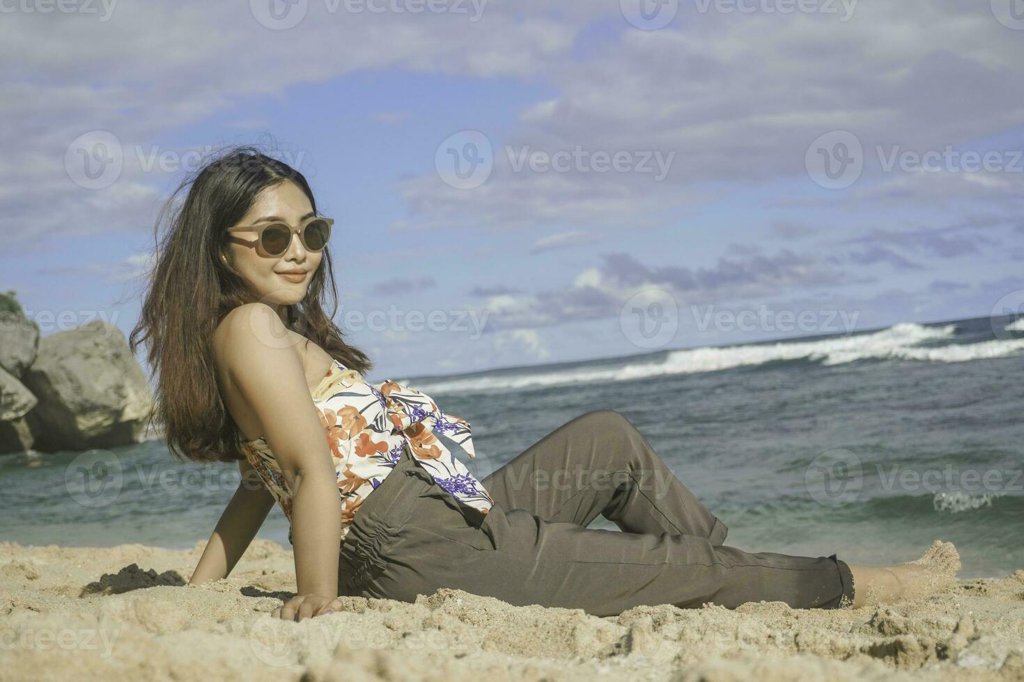 jovem ásia mulher sentar em a de praia areia. retrato sexy ásia senhora viajando e relaxante dentro a verão com tropical natureza. foto