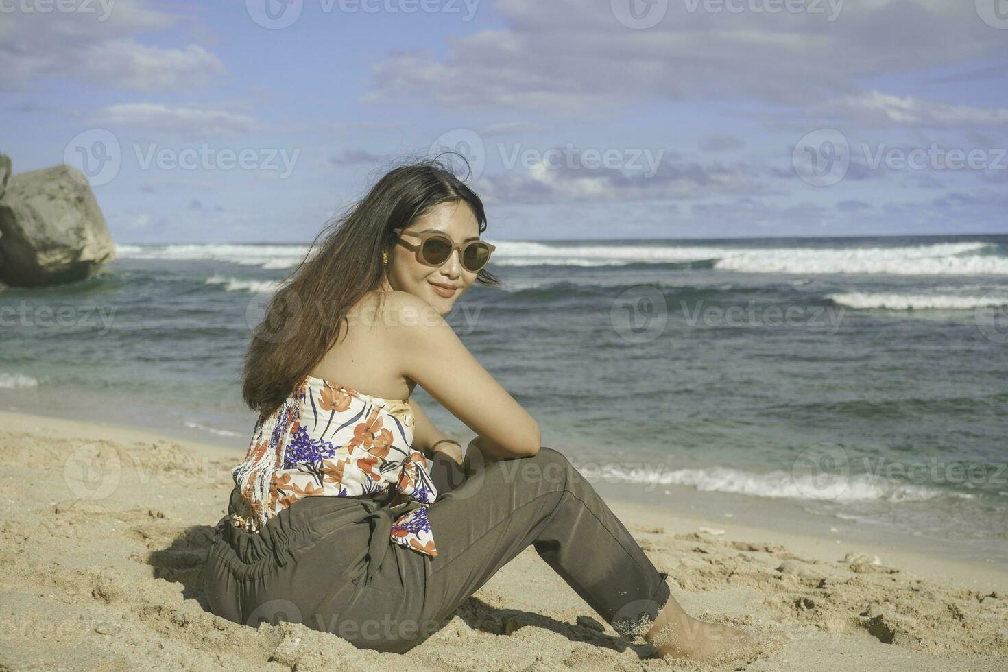 jovem ásia mulher sentar em a de praia areia. retrato sexy ásia senhora viajando e relaxante dentro a verão com tropical natureza. foto