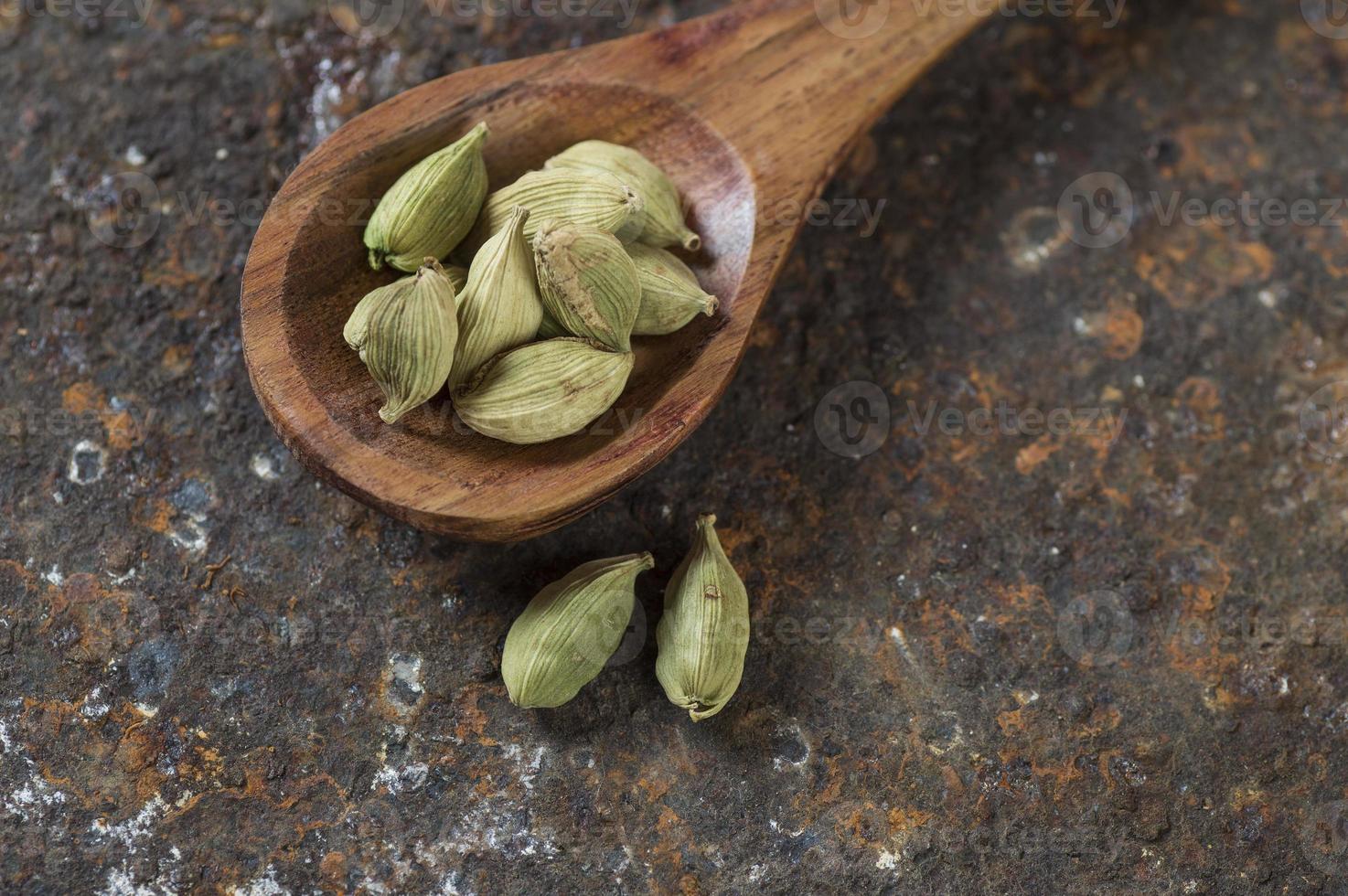 cápsulas de cardamomo em colher de pau em um plano de fundo texturizado foto