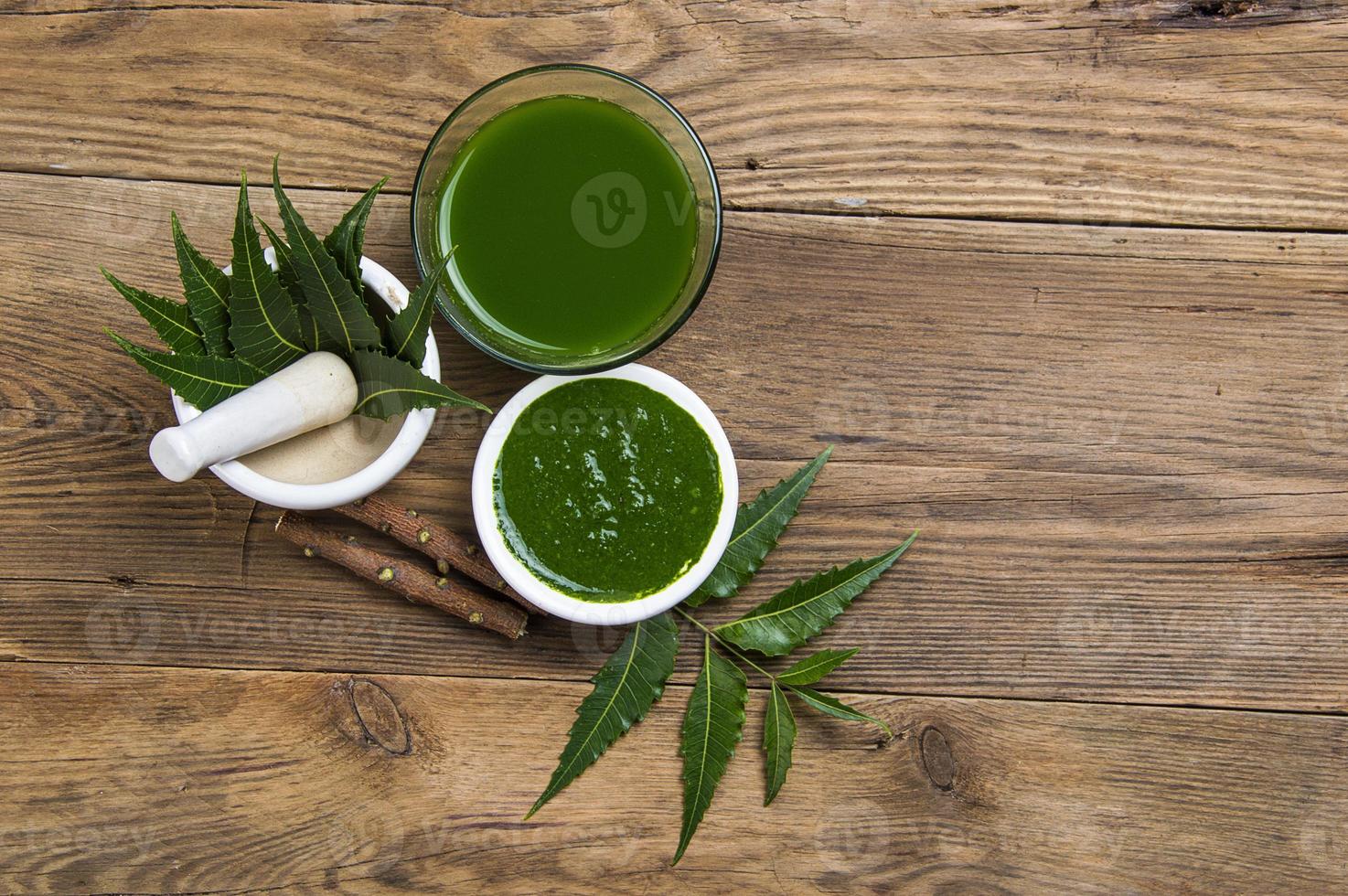 folhas de nim medicinal em almofariz e pilão com pasta de nim, suco e galhos em fundo de madeira foto