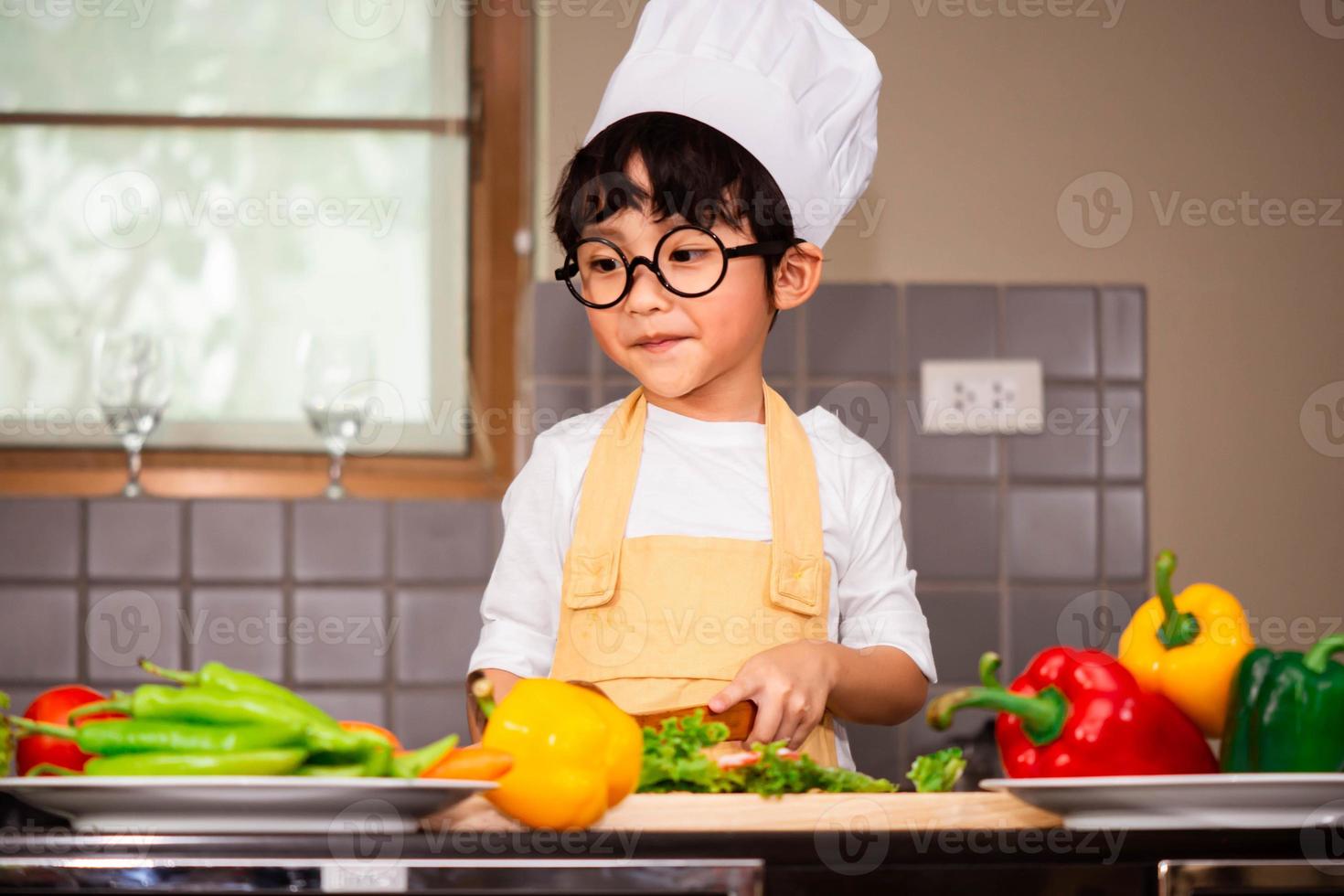 menino asiático cozinhando comida e segurando uma colher de pau foto