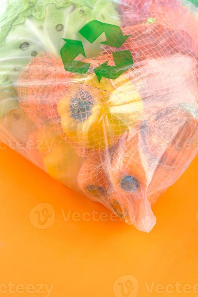 setas recicladas assinam em uma sacola de compras com vegetais em fundo laranja foto