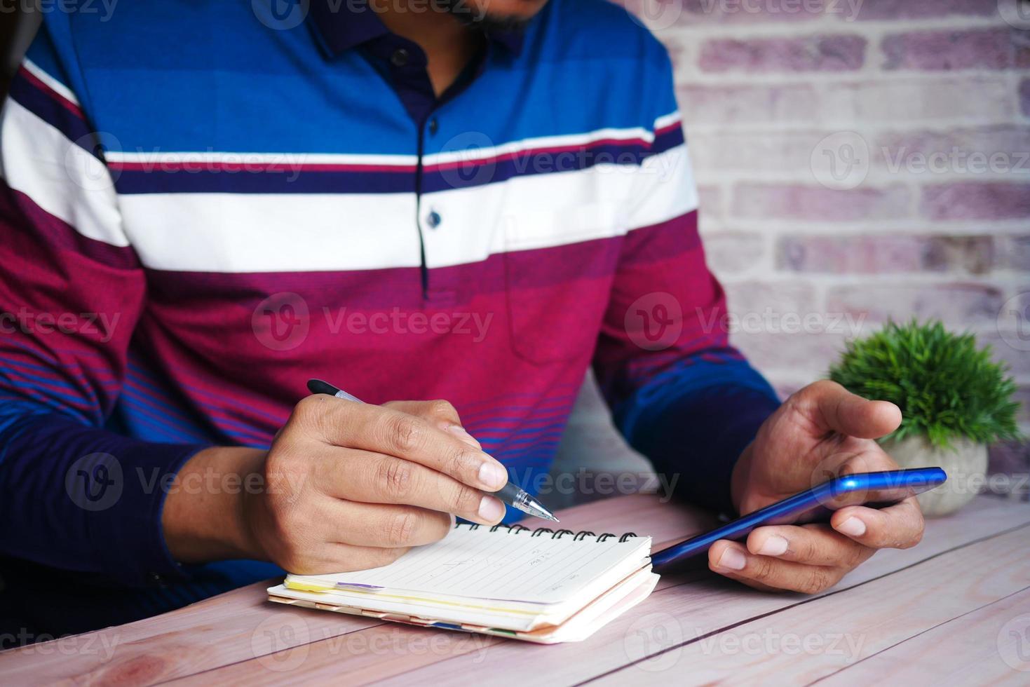 jovem escrevendo à mão no bloco de notas e usando o telefone inteligente enquanto está sentado foto