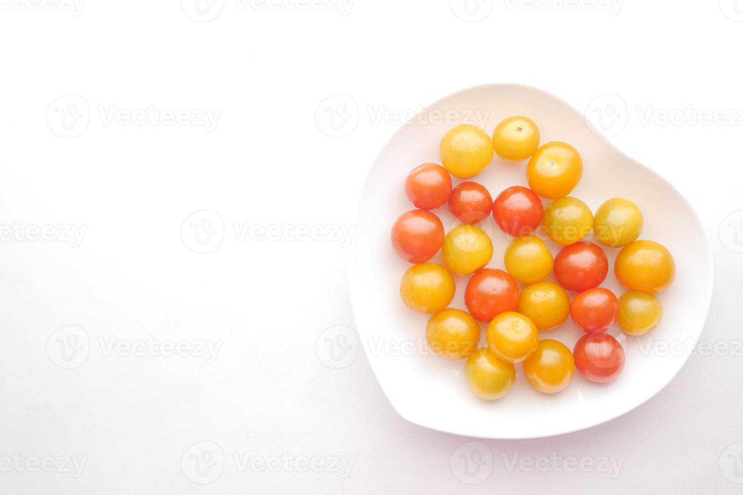 tomate cereja de cor em placa de formato de coração em fundo branco foto