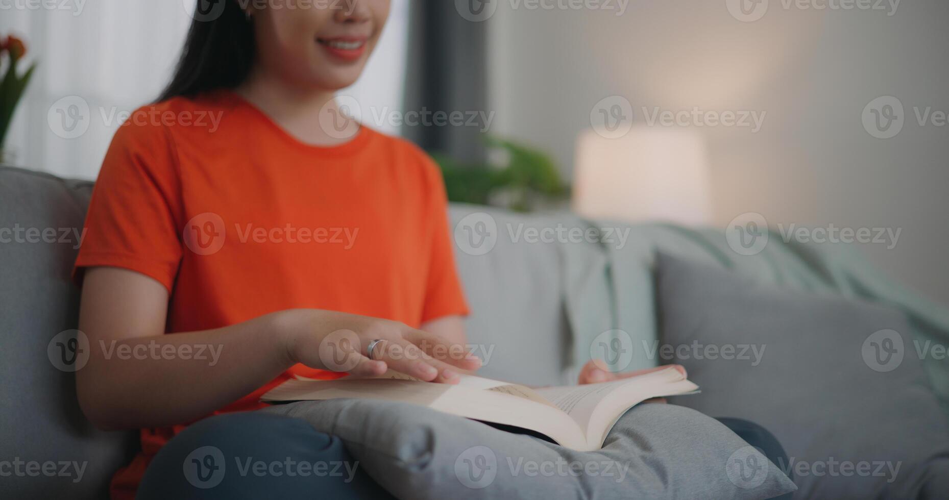 ásia mulher lendo uma livro enquanto sentado em a sofá foto