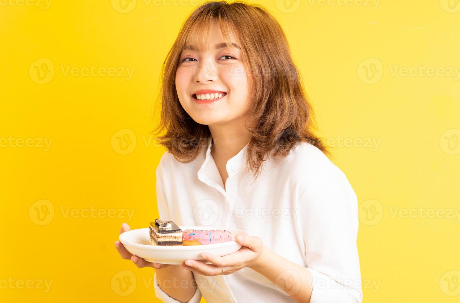 jovem asiática segurando um prato de bolo com uma expressão alegre foto