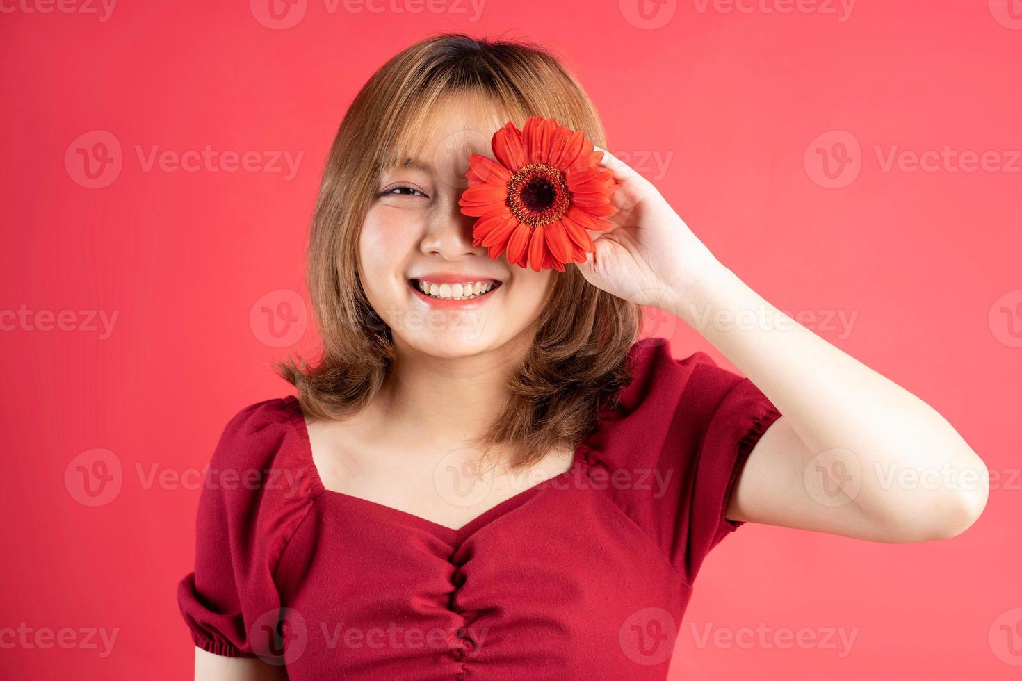 a jovem segurava uma flor gérbera vermelha cobrindo um olho foto